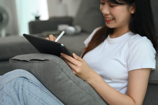 Cheerful asian female freelancer working with digital tablet in living room.