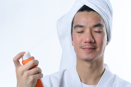 Young man spraying sunscreen on his face. UV protection and aesthetic face treatment concept.