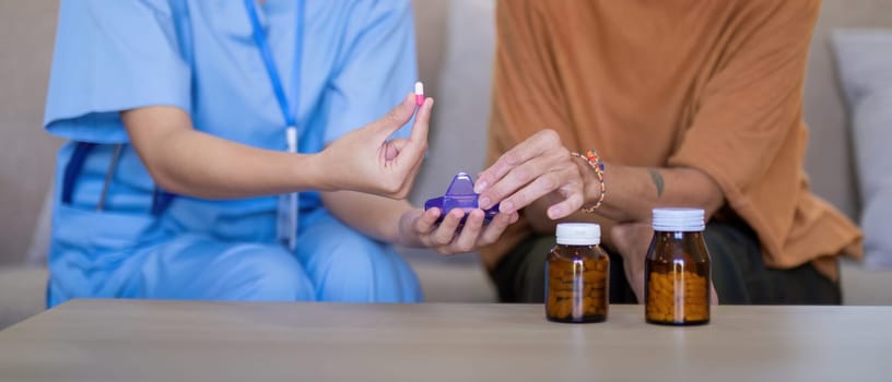 Close up of an Asian caregiver demonstrating medication details to an elderly woman at home, emphasizing elderly care and medication management