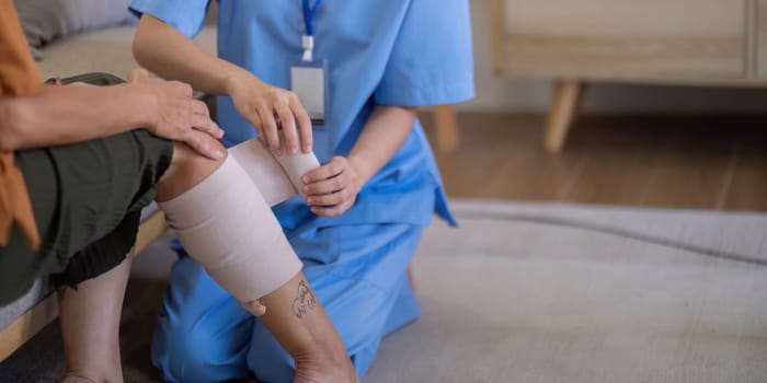 Close up of an Asian caregiver bandaging the leg of an elderly woman at home, focusing on elderly care and wound management