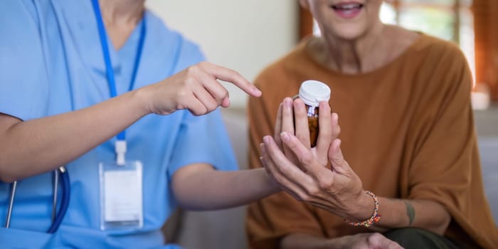 Asian caregiver explaining medication details to an elderly woman at home, emphasizing elderly care and medical guidance