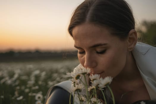 A woman is sitting in a field of white flowers and smelling them. The scene is peaceful and serene, with the sun setting in the background. The woman is enjoying the moment