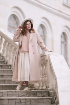 woman in elegant coat and hat against an intricate architectural backdrop, harmoniously blending modern fashion with historical allure. The soft daylight adds to its timeless appeal