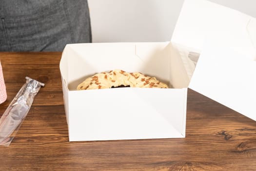 Carefully placing the gingerbread bundt cake, adorned with salted caramel frosting and gingerbread sprinkles, into a white paper bundt cake box with a clear window for gifting.