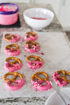 Freshly dipped and still glistening, these crunchy pretzels are lovingly adorned with pink chocolate and a scattering of colorful sprinkles, promising a feast for the senses.