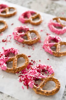 Freshly dipped and still glistening, these crunchy pretzels are lovingly adorned with pink chocolate and a scattering of colorful sprinkles, promising a feast for the senses.