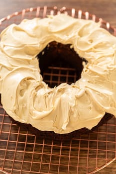 A gingerbread bundt cake being generously frosted with salted caramel frosting and topped with delightful gingerbread sprinkles.