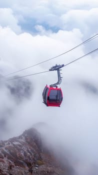 A crimson cable car gracefully ascends over a mountain, traversing the misty sky, creating a picturesque scene