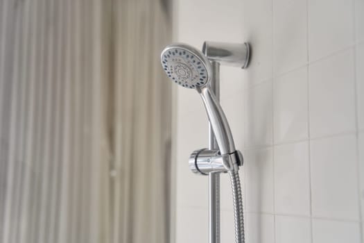 A shower stall with a glass shower door, metal handle, and composite material shower bar featuring a shower head and soap dispenser