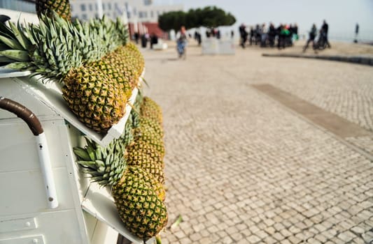 A cart filled with pineapples, a type of terrestrial plant and fruit, on a cobblestone street. The pineapples are a natural whole food, also known as Ananas