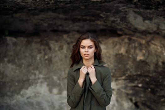 Serene woman in green jacket standing in contemplation before textured rock wall