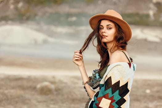 Woman in stylish hat and cozy blanket admiring scenic desert landscape with majestic mountains