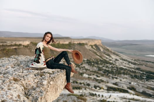 adventurous woman enjoying the view from a cliff with hat and backpack