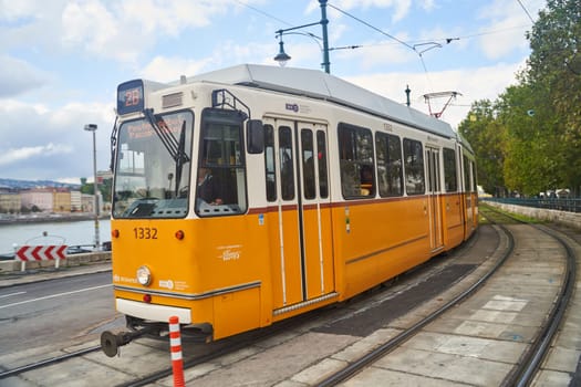 Hungary, Budapest - 04.10.2022: A yellow yellow tram is rolling down the tracks under a sky with fluffy clouds. The electricpowered vehicle is on a journey through nature. Symbol of Budapest