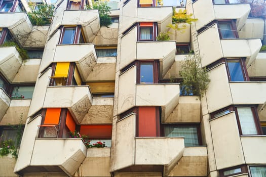 The building boasts numerous windows and balconies, adding character to its facade. Its urban design includes rooftop fixtures and green plants, creating a vibrant apartment complex