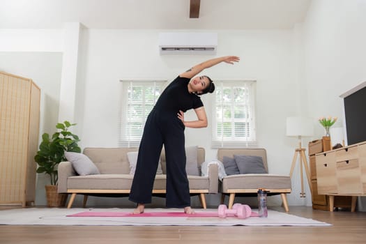 Woman performing a side stretch on a yoga mat in her living room, emphasizing a home workout and flexibility