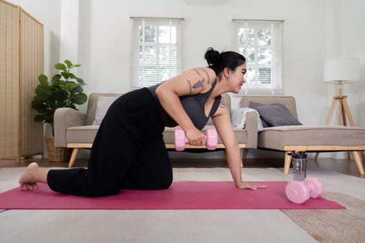 Overweight woman exercising with dumbbells at home, showcasing determination and commitment to weight loss and fitness in a modern living room.