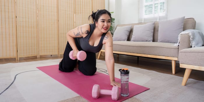 Overweight woman exercising with dumbbells at home, highlighting weight loss journey and commitment to fitness in a cozy living room.