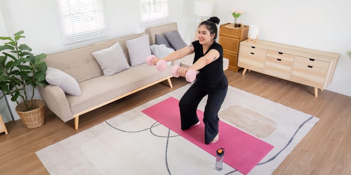 Overweight woman exercising with dumbbells in a modern living room, showcasing weight loss journey and healthy lifestyle.