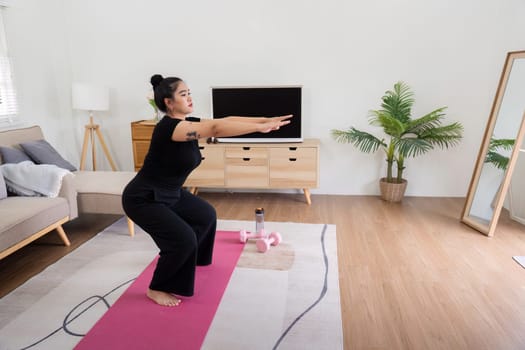 Woman performing squats on a yoga mat in her living room, showcasing a home workout and fitness routine