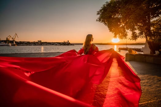 Sunrise red dress. A woman in a long red dress against the backdrop of sunrise, bright golden light of the sun's rays. The concept of femininity, harmony