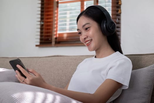 A woman sitting on a sofa, wearing headphones and using her smartphone, embodying the concept of digital leisure and entertainment in a cozy home setting