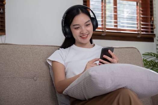 A woman sitting on a sofa wearing headphones and using her smartphone, showcasing the concept of leisure and entertainment in a cozy home environment