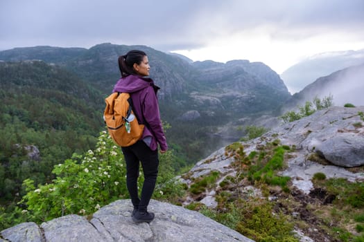 A hiker stands on a rocky precipice overlooking a breathtaking Norwegian fjord, shrouded in mist and clouds. Preikestolen, Norway