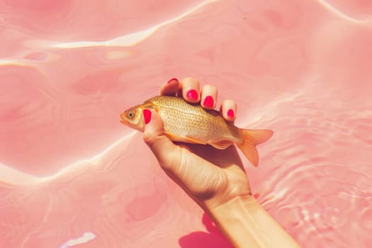 Woman's hand holding goldfish in pool of water with pink background serene beauty of aquatic life
