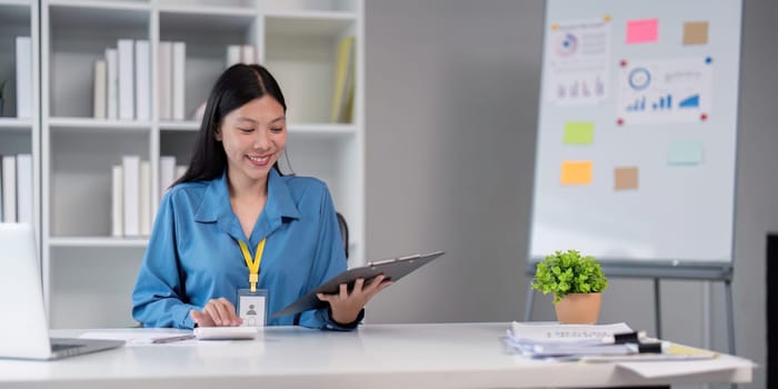 Smiling businesswoman reviewing a clipboard at her desk in a modern office, emphasizing professional analysis and productivity