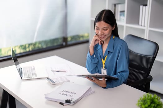 Businesswoman reviewing documents at her desk with a laptop in a modern office, emphasizing professional analysis and productivity