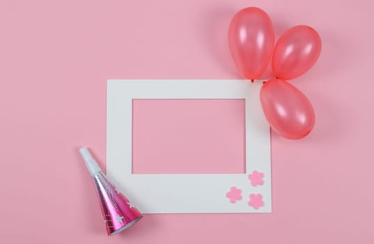 Empty paper frame, three inflated mini balls and one whistle lie on a pink background with copy space in the center, flat lay close-up.