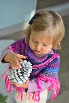 Girl with pine cone at christmas in purple-pink knitted alpaca poncho