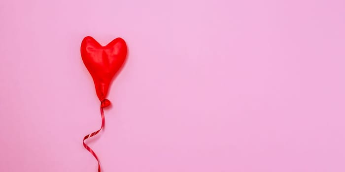 One red deflated heart-shaped balloon lies in the left on a pink background with copy space on the right, flat lay close-up.