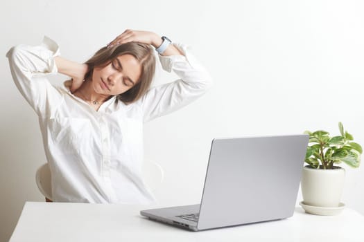 A girl does exercises in front of a laptop after a long day of work, stretches her neck, pain in the head and neck from sedentary work
