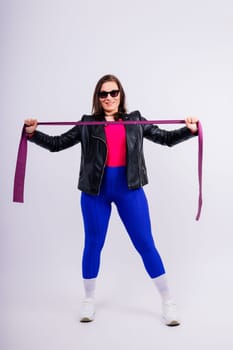 Strong female working with resistance band. Photo of model in fashionable sportswear on grey background.