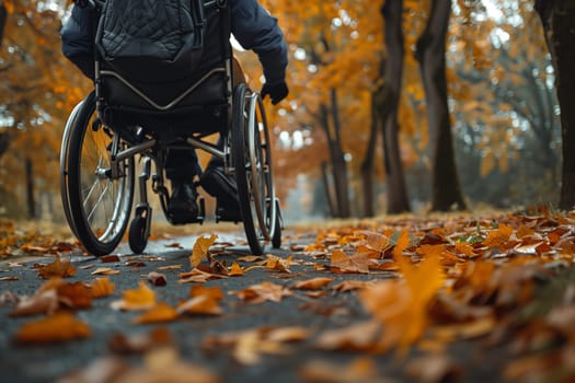 A person in a wheelchair moves along a path lined with fallen autumn leaves. The path is shaded by trees with orange and yellow leaves.