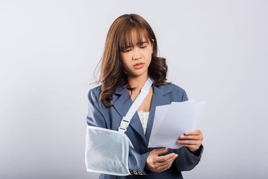 Depressed upset businesswoman arm in a splint after an accident, finds comfort in sling support from an excited while holding medical bills payment. Asian woman on white background, Broken arm