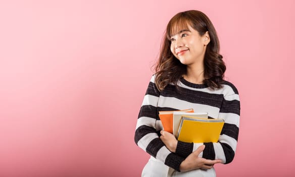 Portrait of beautiful Asian young woman teenage smiling hugging books, female person holding book multicolor, studio shot isolated on pink background with copy space, education concept