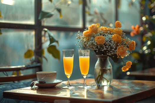 A table setting with two glasses of orange juice, a vase of yellow flowers, and a small white cup and saucer.