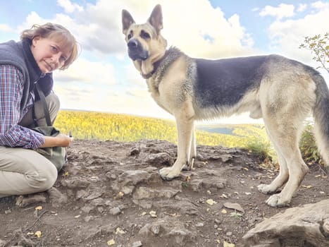 Adult girl or middle aged woman with shepherd dog on top of mountain. Walk on nature. Tourist and travel