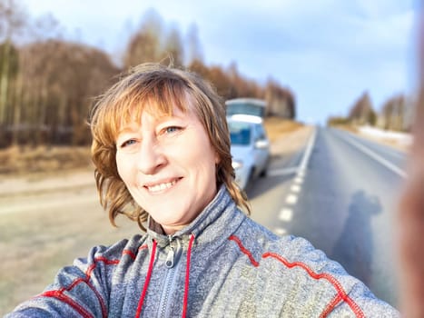 A woman takes a selfie on the road near a car. The concept of car travel. A woman captures a selfie with her car in the background during road trip