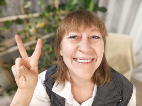 Portrait of a middle-aged woman taking selfie in a room with plants and flowers. Blogger and online streaming