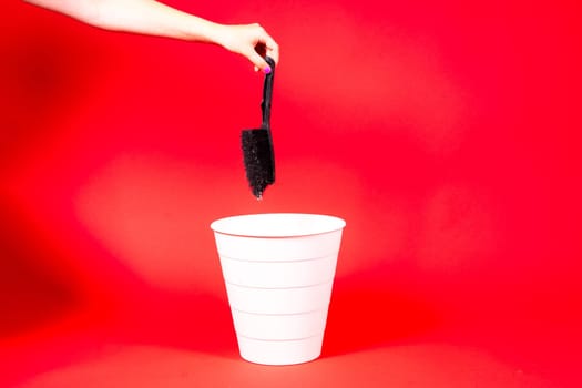 Hand throws brush into trash bin with package on a red background