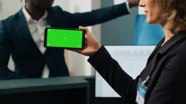 Store worker using smartphone with greenscreen template at cash register, working on commercial activity with male customer. Female employee looks at chromakey layout and copyspace. Camera A.