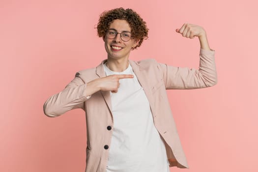 I am strong and independent. Caucasian curly haired man in jacket showing biceps and looking confident, feeling power strength to fight for rights, energy to gain success win. Guy on pink background
