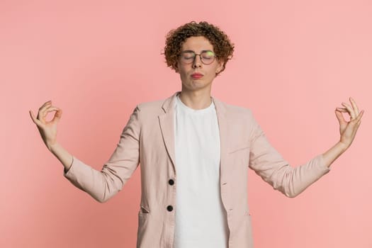 Keep calm down, relax, inner balance. Young man breathes deeply with mudra gesture, eyes closed, meditating with concentrated thoughts, peaceful mind. Attractive guy isolated on pink background