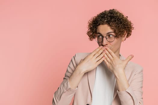 I will not say anything. Concentrated curly haired man closing mouth with hands, looking intimidated scared at camera gestures no refusing to tell terrible secret unbelievable truth on pink background