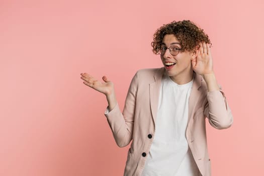 I can't hear you. What. Caucasian man trying hear you looking confused and frowning keeping arm near ear for louder voice asking to repeat, to hear information deafness. Young guy on pink background