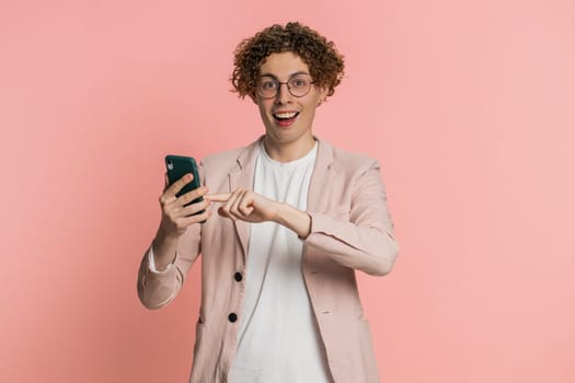 Caucasian man texting share sms messages content on smartphone social media applications online, watching relax movie browsing. Young guy uses mobile phone smile isolated on pink background indoors